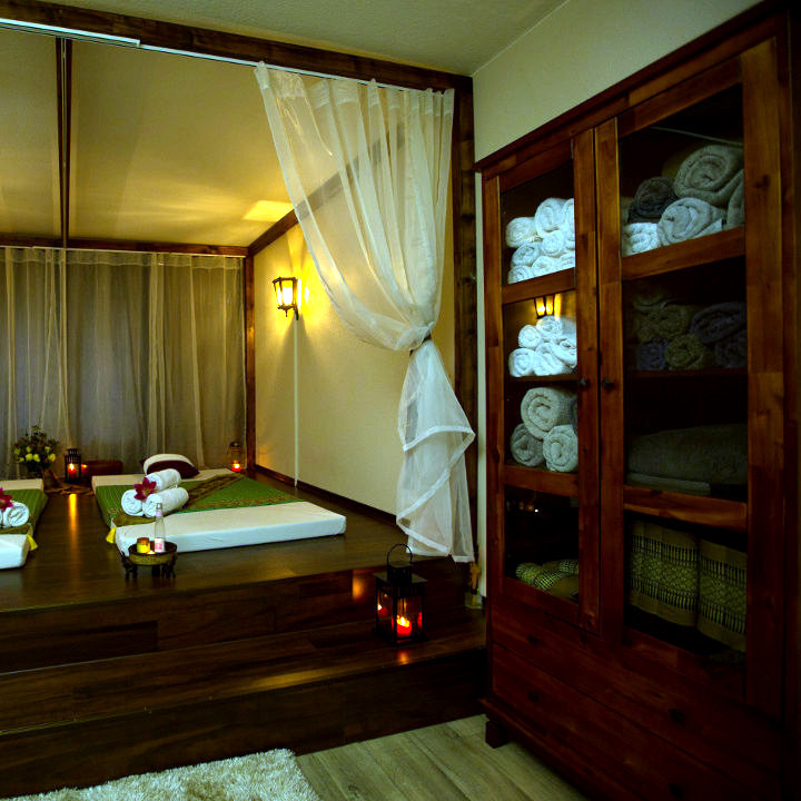 Behandlungszimmer mit Massageliege, Vorhang und Holzschrank voller frischer Tücher