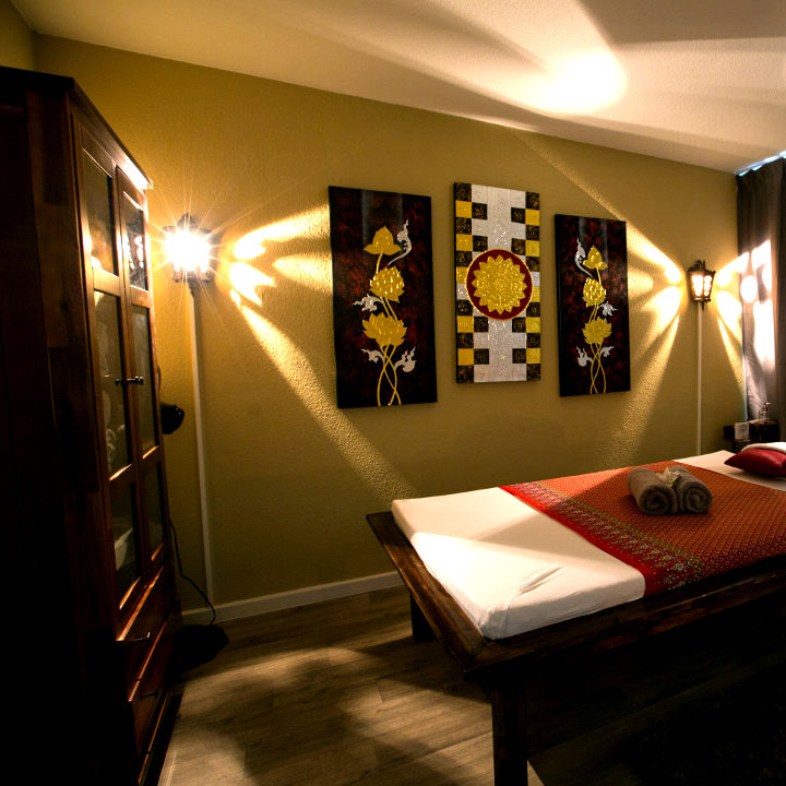 Behandlungszimmer mit drei Lotusbildern an der Wand und Massageliege im warmen Licht